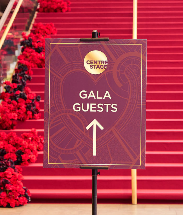 Centre Stage Gala branded event signage with gold logo and art deco design directing guests up the rose-lined red carpet staircase